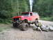1989 Ford Bronco - A red Ford Bronco navigates an obstacle course on a dirt road surrounded by trees.