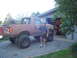1989 Ford Bronco - A man stands beside a heavily modified, older model Ford Bronco, parked in front of a suburban garage.
