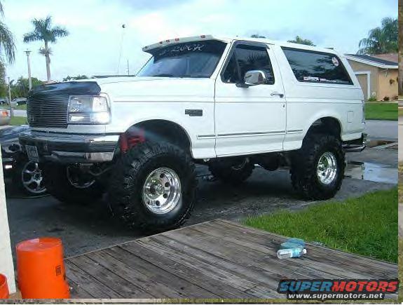 White lifted Ford Bronco with aftermarket wheels and tires, parked on a wooden deck