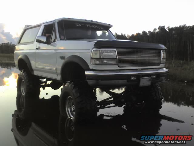 White lifted Ford Bronco with aftermarket grille, parked in shallow water