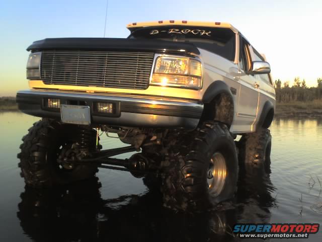 White 1995 Ford Bronco with large tires in water, D-ROCK decal on windshield
