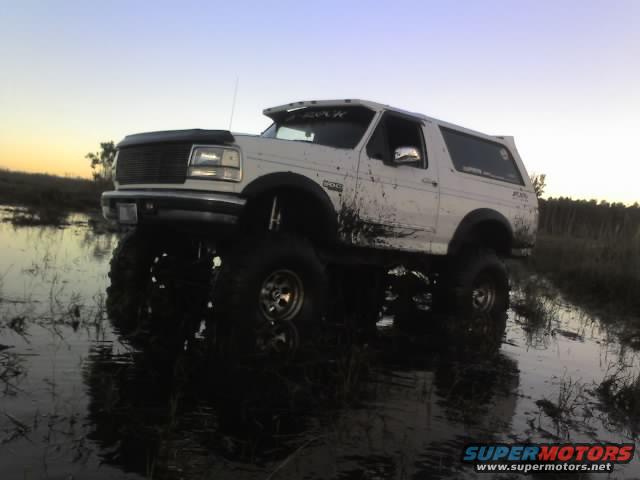 White Bronco with large tires stuck in mud. It has a lift kit and mud splattered on the side