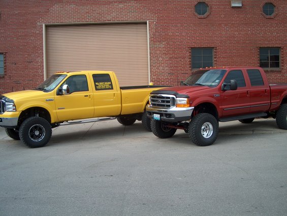 Yellow and red lifted pickup trucks parked outside a brick building with a large garage door