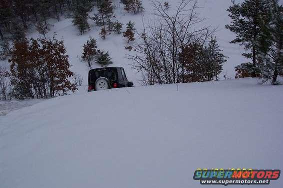 Black Jeep Wrangler in deep snow on a wooded hillside