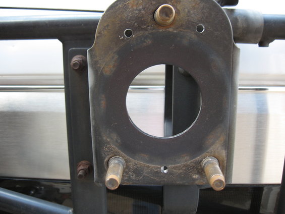 Rusty metal spare tire carrier mount with a large central hole and two protruding bolts