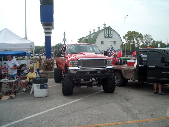 Lifted red pickup truck with large tires parked next to a black truck. American and Confederate flags are on the truck bed