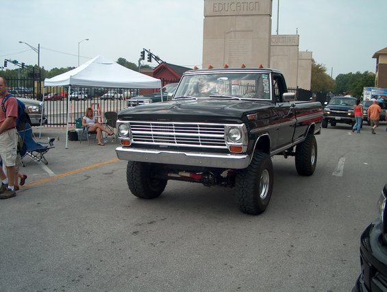 black lifted pickup truck with chrome grille and dual headlights, people in background