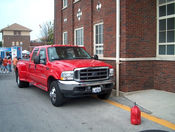 Red Ford F-350 Super Duty pickup truck parked next to a brick building, front 3/4 view