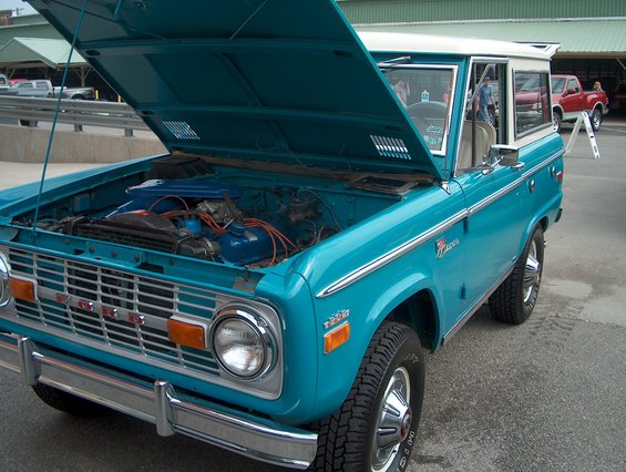 Turquoise 1978 Ford Bronco with hood open, showing engine. Chrome grille and bumpers. White roof