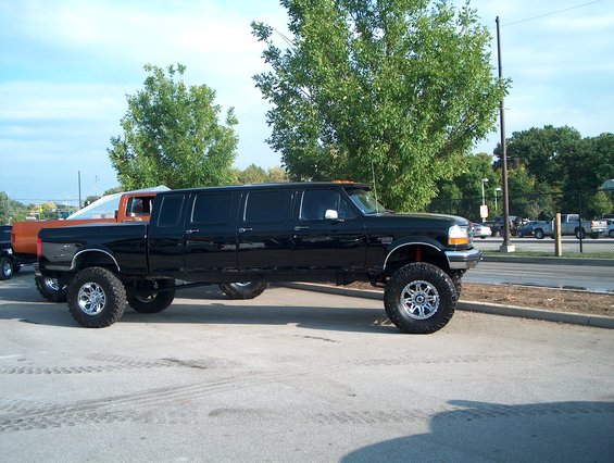 Black stretched pickup truck with lifted suspension and large tires parked on asphalt