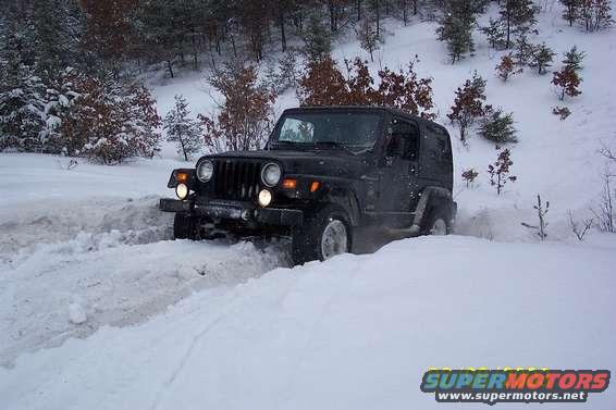 black Jeep Wrangler driving through deep snow on a wooded hill