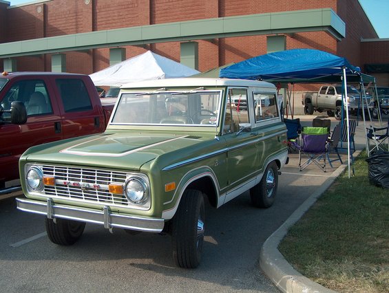 Green 1978 Ford Bronco parked next to a red pickup truck, with tents and chairs in the background