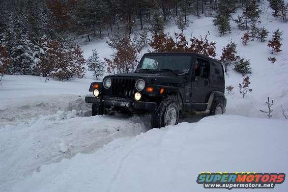 Black Jeep Wrangler driving through snow, front quarter view