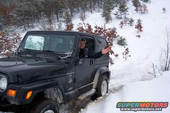 Black Jeep Wrangler driving through snow with driver waving