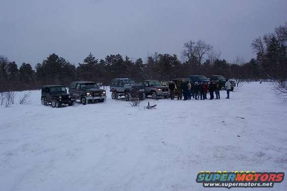Several SUVs and trucks parked in a snowy field with trees in the background
