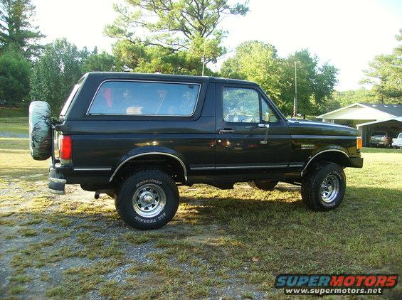 Black 1990 Ford Bronco parked on gravel with trees and house in background