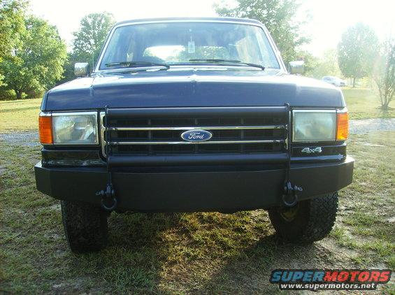 Dark blue Ford Bronco front view with a black bull bar and chrome grille. "4x4" badge visible