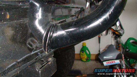Black metal pipe attached to fender, with a bottle of cleaner and a seat in the background