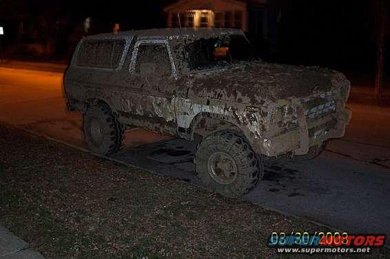 Mud-covered 1978 Ford Bronco from the front-right, parked on a street at night