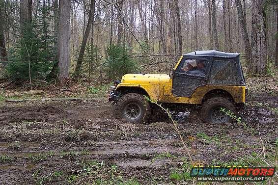 Yellow Jeep CJ-5 stuck in mud on a wooded trail. Soft top is black