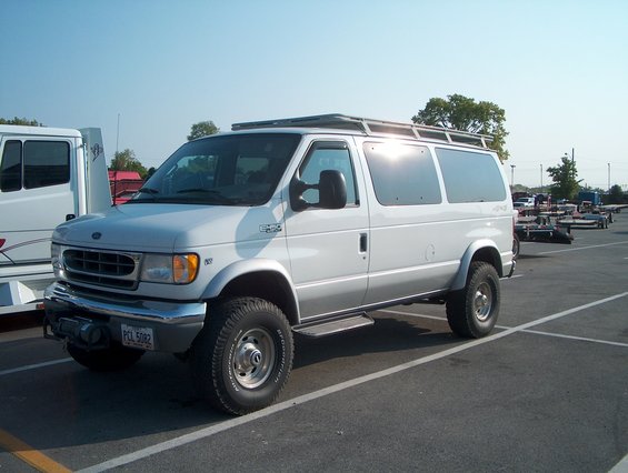 White Ford E-Series van with roof rack and off-road tires parked in a lot