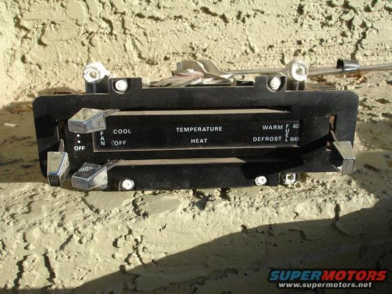 Black car climate control panel with chrome knobs and labels for temperature, fan speed, and defrost