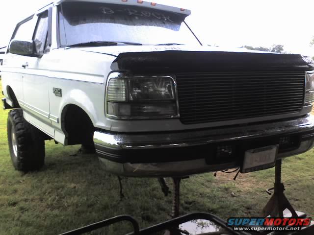1995 Ford Bronco front end lifted on jack stands, black grille, hood cover on
