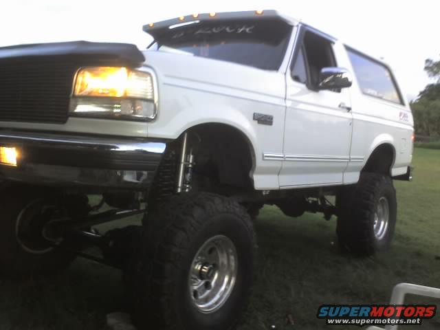 White 1995 Ford Bronco with large tires and lifted suspension. The front end is visible with headlights on