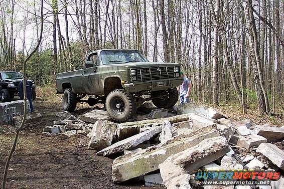 Olive green pickup truck with large tires on a rocky obstacle course