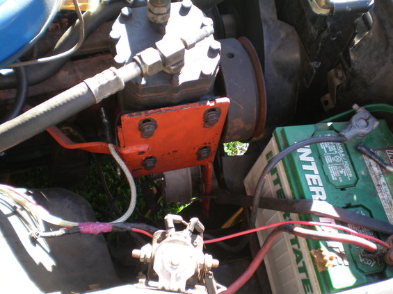 Engine bay with green Interstate battery, orange bracket, and air conditioning compressor