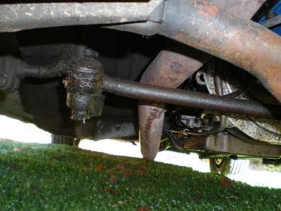 Underside view of a greasy steering linkage and exhaust pipe on a vehicle