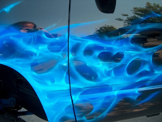 Dark vehicle side with bright blue flame airbrushing. A person is reflected in the upper left