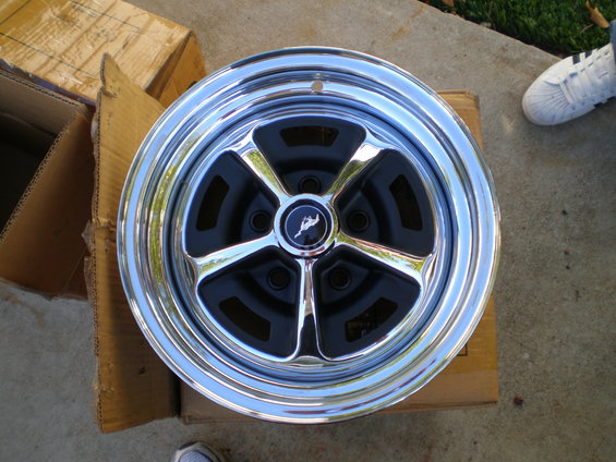 Chrome five-spoke wheel with black inserts and a running horse emblem in the center. It looks like a 1966 Ford Mustang wheel