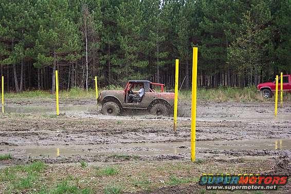 Brown 1978 Ford Bronco driving through mud obstacle course with yellow poles
