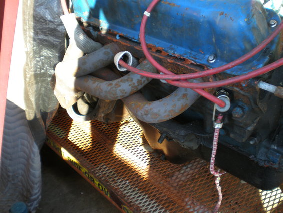 Engine with blue valve covers and rusty exhaust manifolds on a metal platform