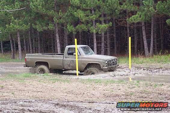 Pickup truck stuck in mud with trees in background. Two yellow poles are visible