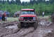 1989 Ford Bronco - Off-road vehicles, including a red 1989 Ford Bronco, tackle a muddy course during an event.