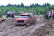 1989 Ford Bronco - A red SUV navigates a muddy track during an off-road event, with spectators and other vehicles present.