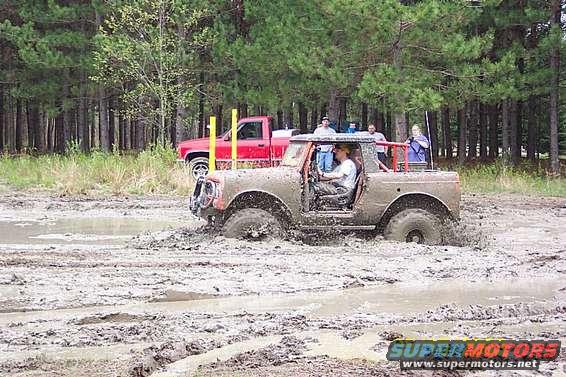 Mud-covered off-road vehicle with open doors in a muddy field, driver visible