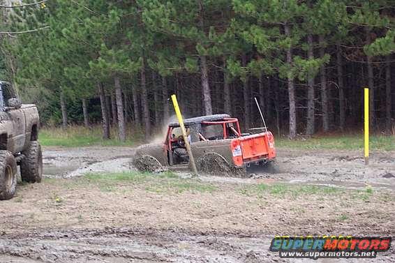 Orange off-road vehicle stuck in mud pit with another truck nearby