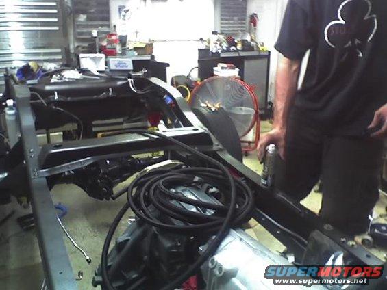 Vehicle frame with engine and transmission visible, undergoing work in a garage