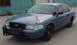 1998 Ford Crown Victoria - A blue sedan with a push bumper is parked in front of a teal building.