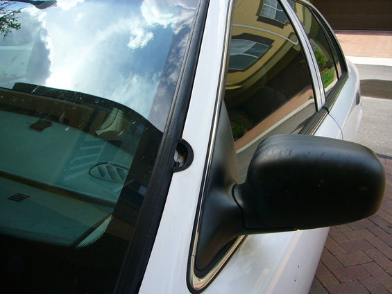 Close-up of a car's side mirror and part of the windshield. Building reflected in the window