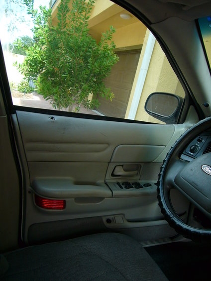 Interior view of a Ford Crown Victoria, showing the driver's side door panel, steering wheel, and a tree outside the window