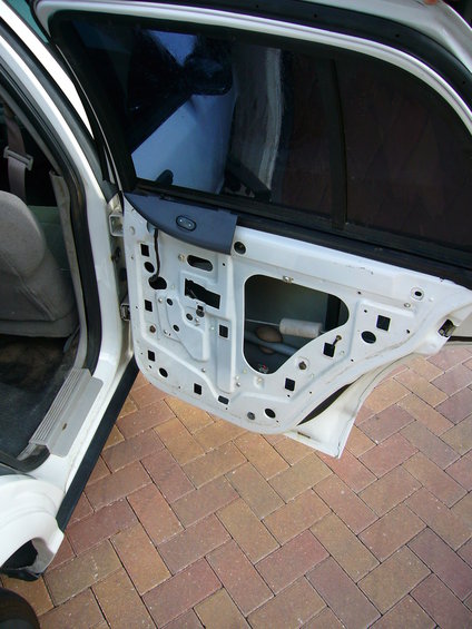 Interior of a white car door frame with the door panel removed, showing internal structure and window mechanism
