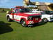 1988 Ford Sport - A red and white tow truck is parked on a grassy field next to other vehicles and a large aircraft.
