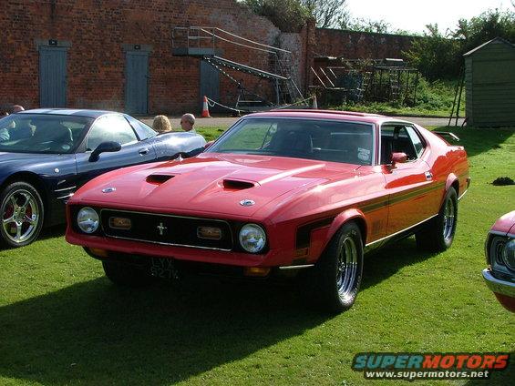 Red 1971 Ford Mustang Mach 1 parked on grass next to a blue car
