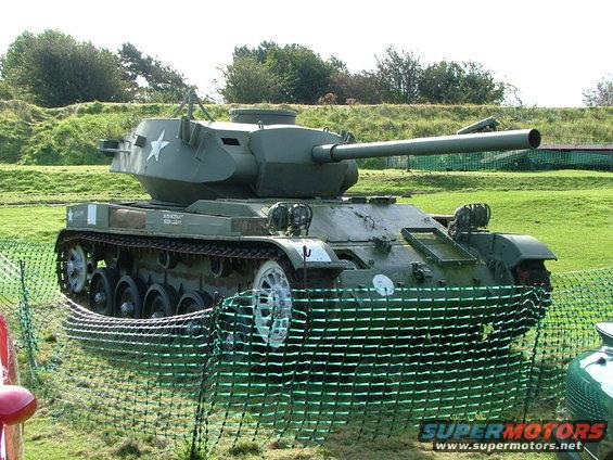 Green military tank with a star emblem on the turret, behind a green fence