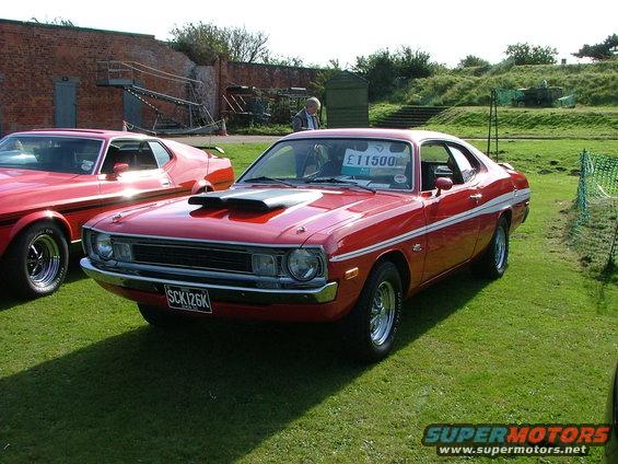 Red coupe with white side stripe, hood scoops, and chrome wheels. License plate SCK126K