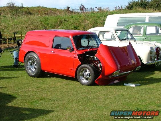 Red van with hood open, drag racing tires, parked on grass next to other cars